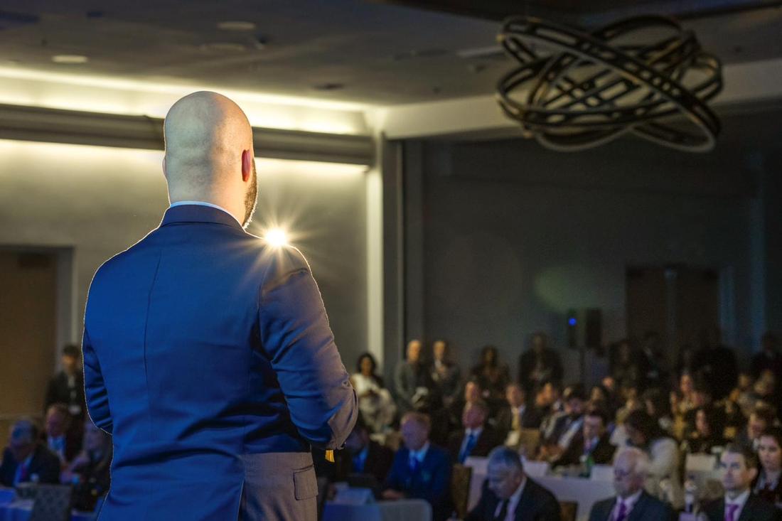 Lukas Schulte seen from behind on stage, speaking to a packed conference room