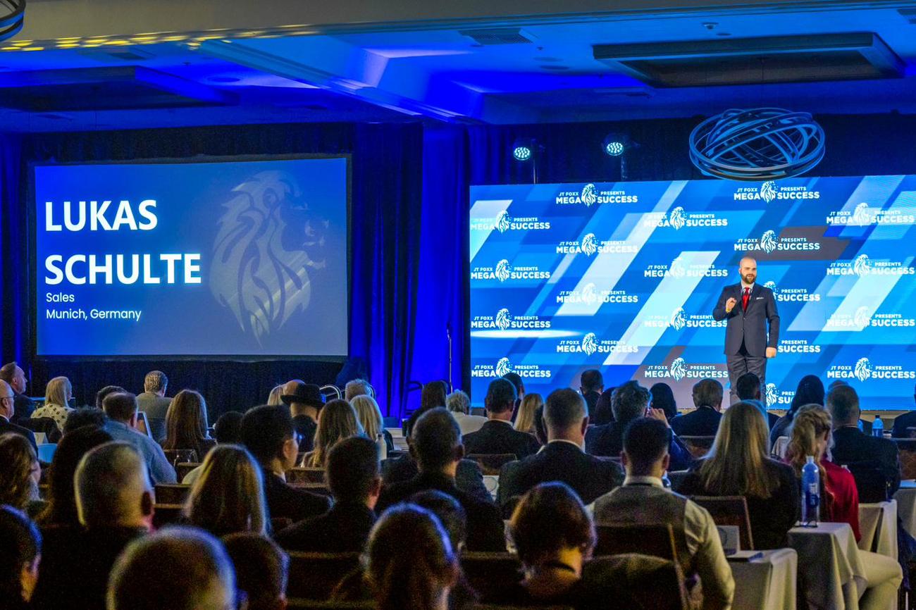 Lukas Schulte speaking on a large stage in front of a full conference audience