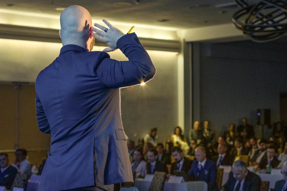 Lukas Schulte seen from behind, addressing a packed conference room