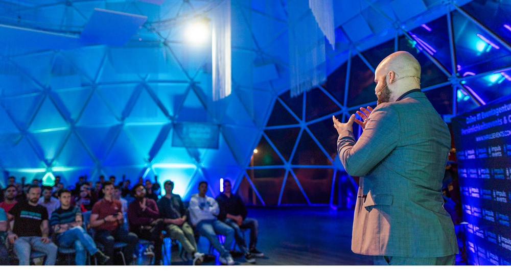 Lukas Schulte speaking to an audience in a blue-lit dome venue